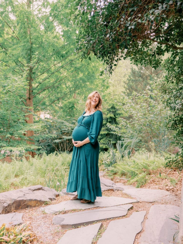 Mother-to-be smiling among lush greenery during a natural light maternity session at Duke Gardens in Durham, North Carolina