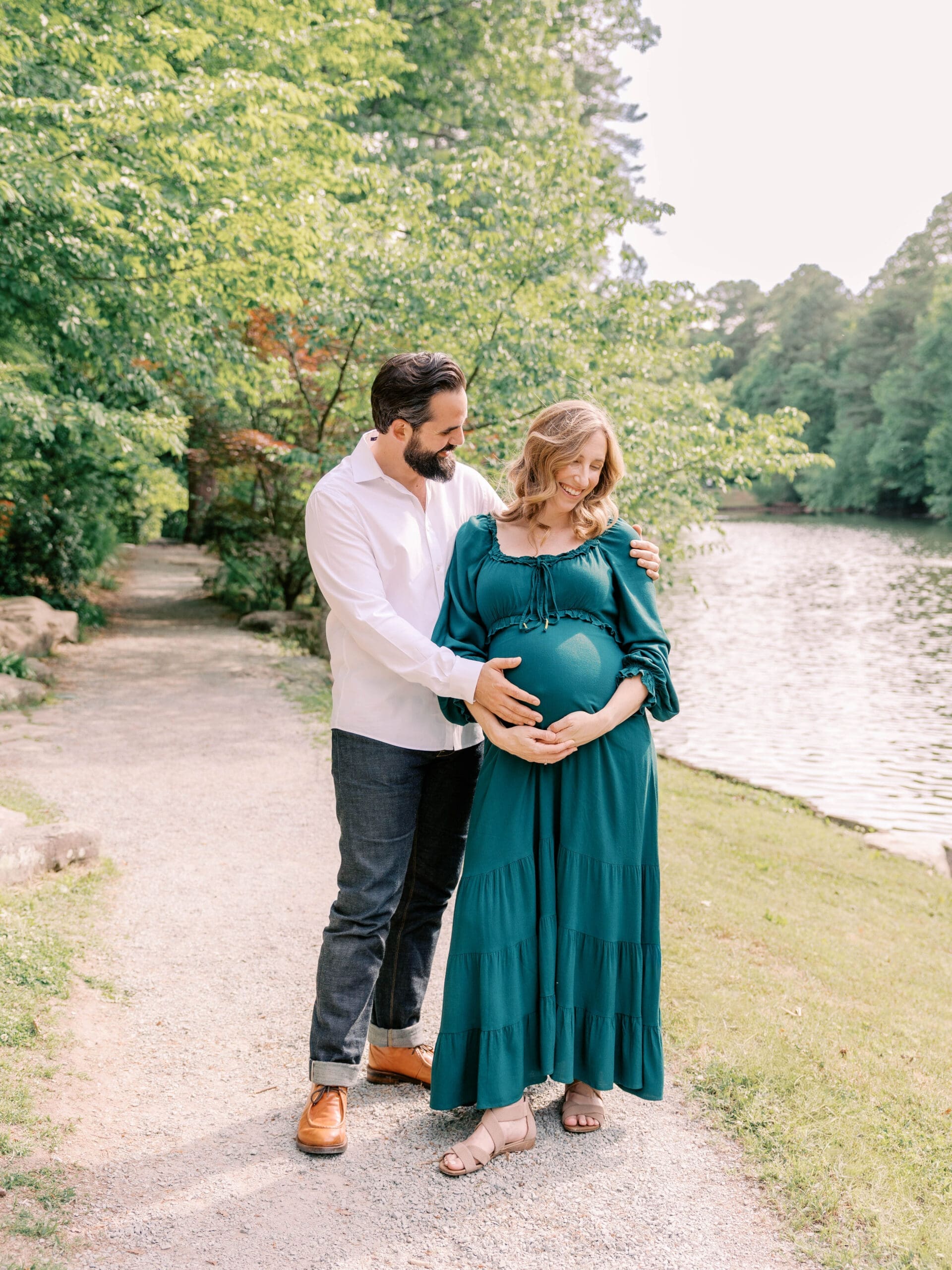 Expecting parents embracing by the water during a spring maternity photography session at Duke Gardens in Durham, North Carolina