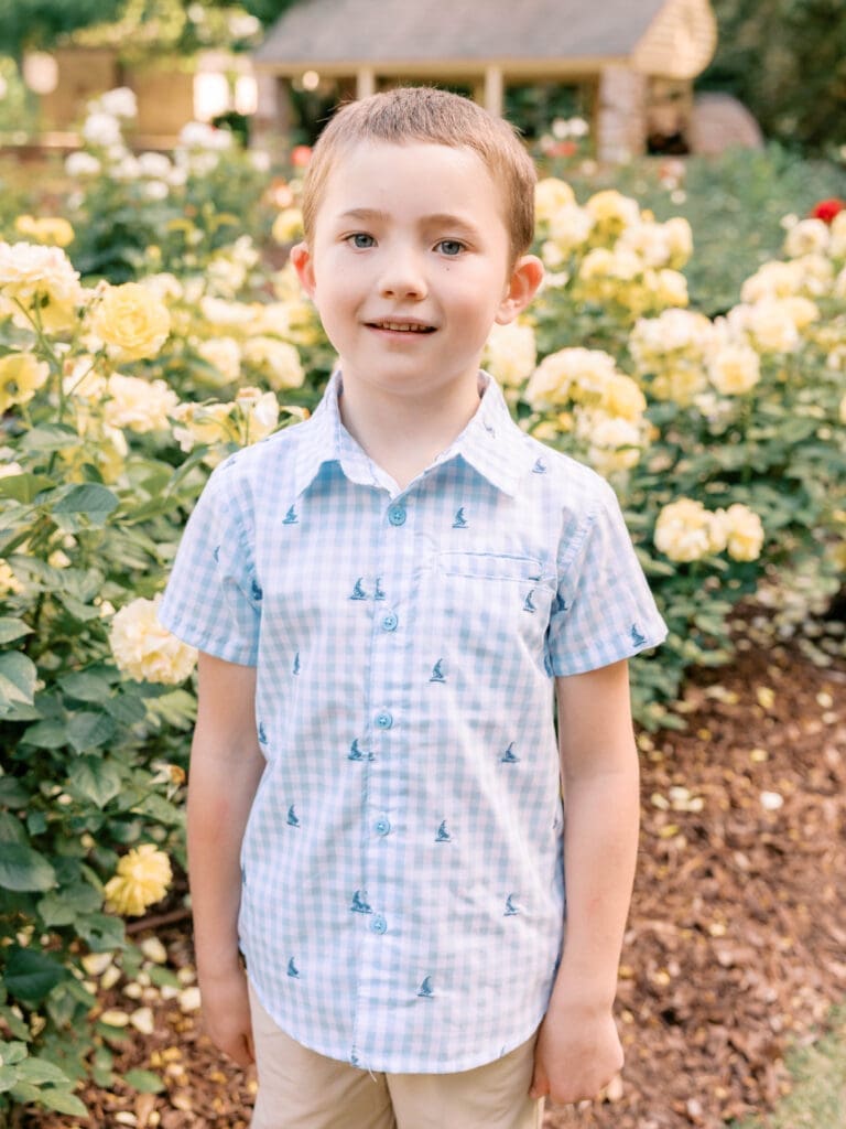 Older brother smiling among blooming roses during a family maternity photography session in Raleigh