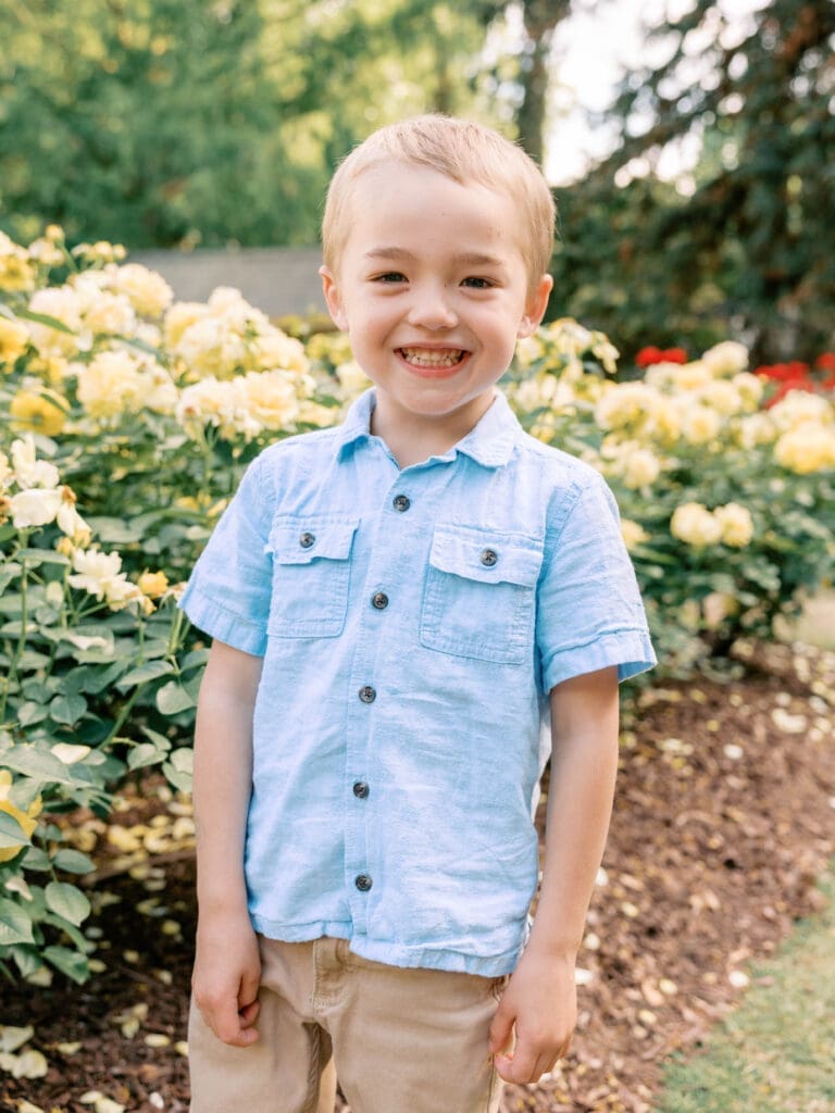 Smiling toddler boy standing among yellow roses during a Raleigh Rose Garden family maternity session