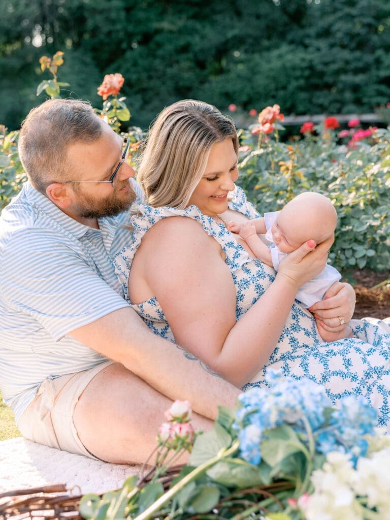 New parents sitting together with their newborn son surrounded by blooming roses in Raleigh.
